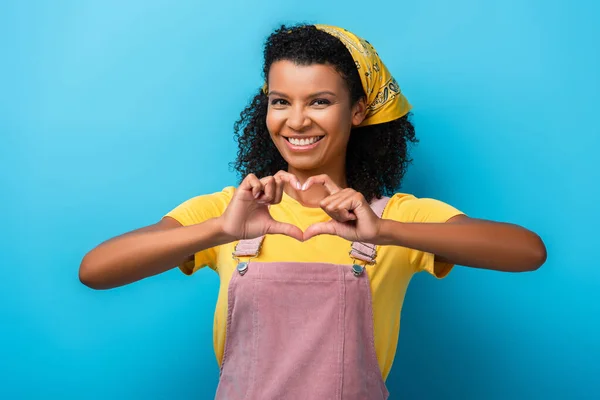 Cheerful african american woman showing heart sign with hands on blue — Stock Photo