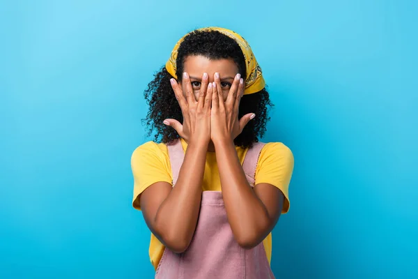 Afroamerikanerin bedeckt Gesicht mit Händen auf blauem Grund — Stockfoto