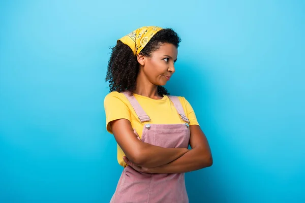 Femme afro-américaine sceptique debout avec les bras croisés et regardant loin sur le bleu — Photo de stock