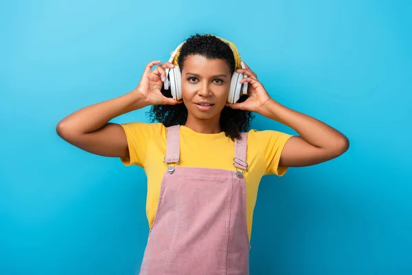 Mujer afroamericana en auriculares inalámbricos escuchando música en azul - foto de stock