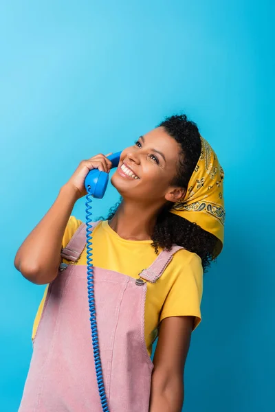 Счастливая африканская женщина разговаривает по ретро-телефону на голубом — стоковое фото