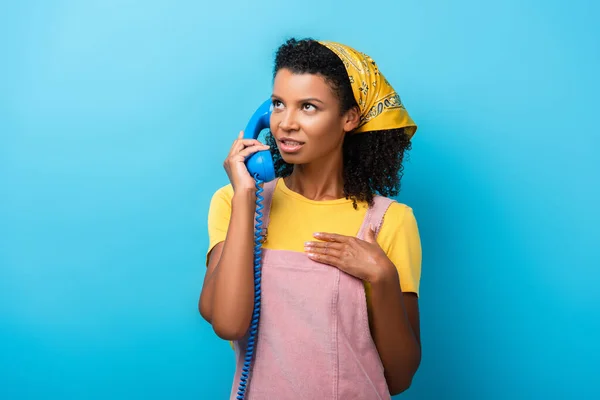 Curly african american woman talking on retro telephone on blue — Stock Photo