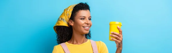 Smiling african american woman looking at reusable mug on blue, banner — Stock Photo