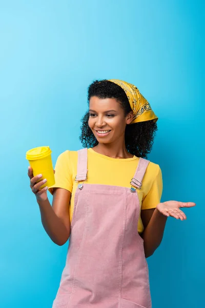 Mujer afroamericana feliz sosteniendo taza reutilizable en azul - foto de stock