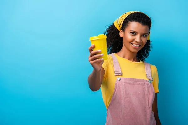 Fröhliche afrikanisch-amerikanische Frau hält Mehrwegbecher auf blau — Stockfoto