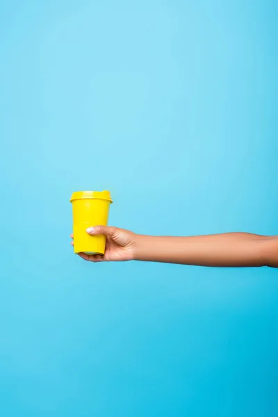 Vista parcial de mujer afroamericana sosteniendo taza reutilizable aislada en azul - foto de stock