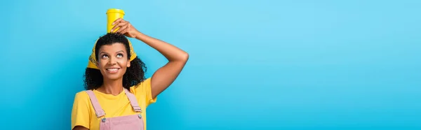 Felice donna afroamericana che tiene una tazza riutilizzabile sopra la testa su blu, banner — Foto stock