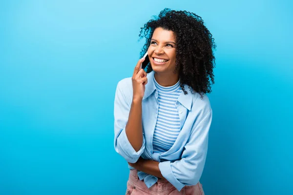 Mujer afroamericana feliz hablando en el teléfono inteligente en azul - foto de stock
