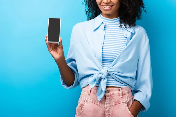 Vista cortada de mulher americana africana feliz segurando smartphone com tela em branco no azul — Fotografia de Stock