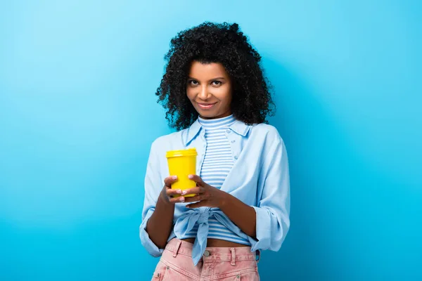 Pleased african american woman holding empty reusable mug on blue — Stock Photo