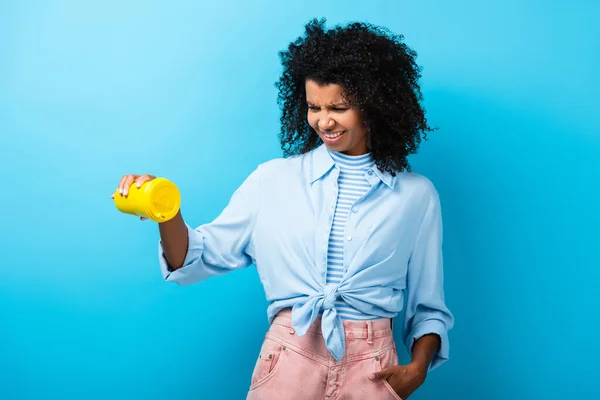 Femme afro-américaine insatisfaite tenant vide tasse réutilisable sur bleu — Photo de stock