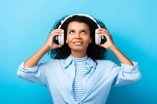 Happy african american woman listening music in headphones on blue — Stock Photo