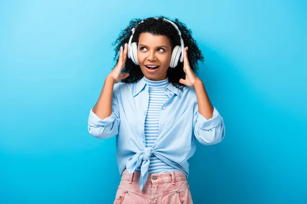 Excité femme afro-américaine écouter de la musique dans les écouteurs sur bleu — Photo de stock