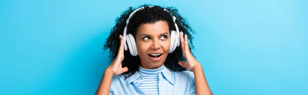 Animado afro-americano mulher ouvindo música em fones de ouvido em azul, banner — Fotografia de Stock