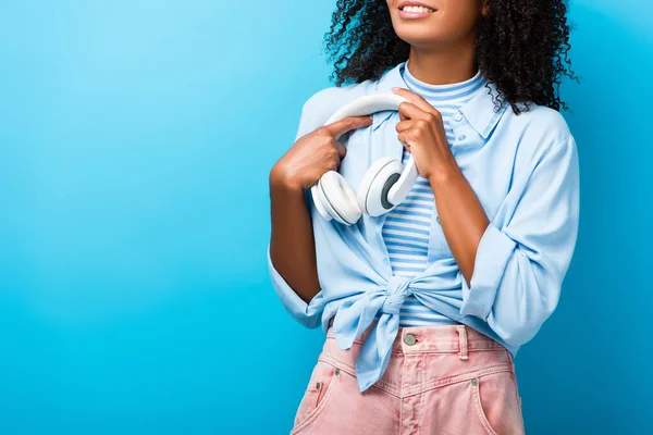 Vue recadrée de heureuse femme afro-américaine tenant des écouteurs sur bleu — Photo de stock