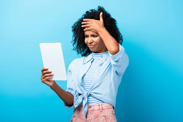 Displeased african american woman looking at digital tablet on blue — Stock Photo