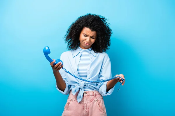 Засмучена афро-американська жінка, яка тримає ретро-телефон на синій — стокове фото