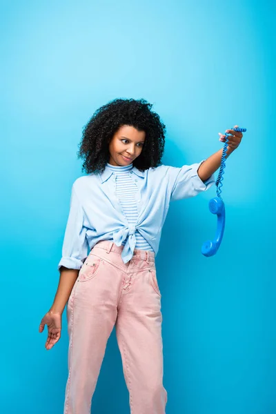 Femme afro-américaine déçue tenant téléphone rétro sur bleu — Photo de stock