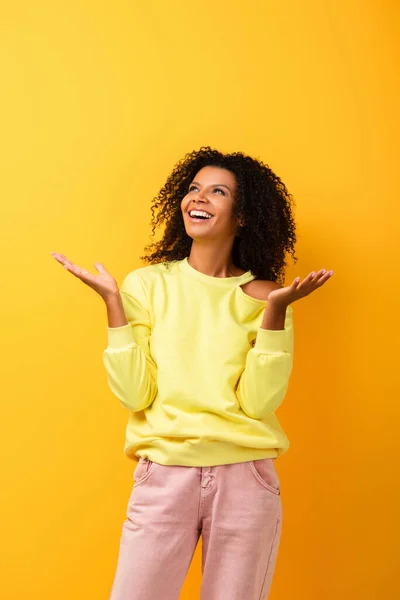 Mujer afroamericana emocionada mirando hacia arriba y haciendo gestos en amarillo - foto de stock