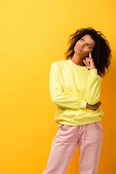 Pensive african american woman looking away while thinking on yellow — Stock Photo