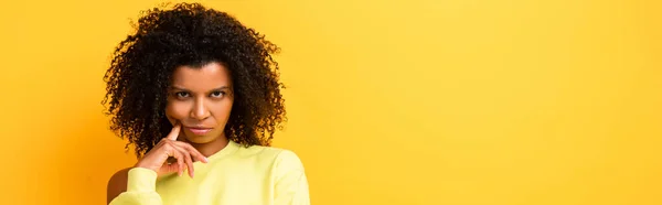 Mujer afroamericana seria mirando la cámara en amarillo, pancarta - foto de stock