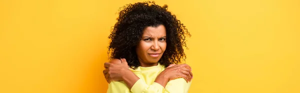 Mujer afroamericana disgustada abrazándose en amarillo, bandera - foto de stock