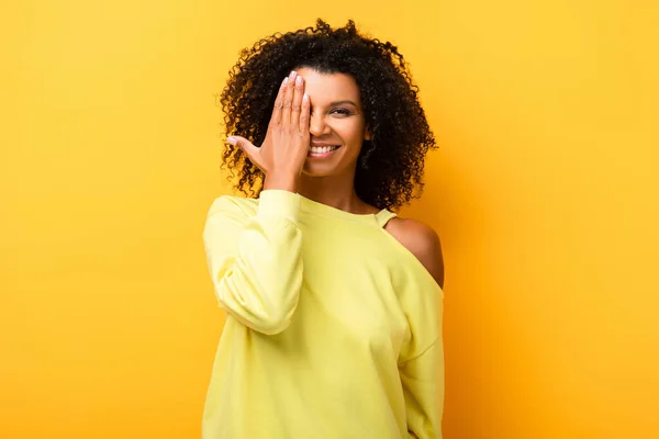 Heureuse afro-américaine femme couvrant oeil sur jaune — Photo de stock