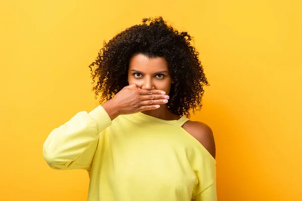 African american woman covering mouth and looking at camera on yellow — Stock Photo
