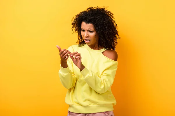 Femme afro-américaine mécontente regardant les doigts sur jaune — Photo de stock