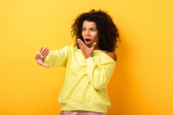 Impactado mujer afroamericana mirando clavos en amarillo - foto de stock