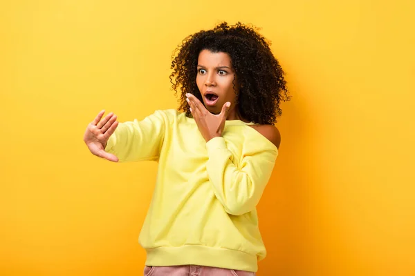 Impactado mujer afroamericana mirando clavos en amarillo — Stock Photo