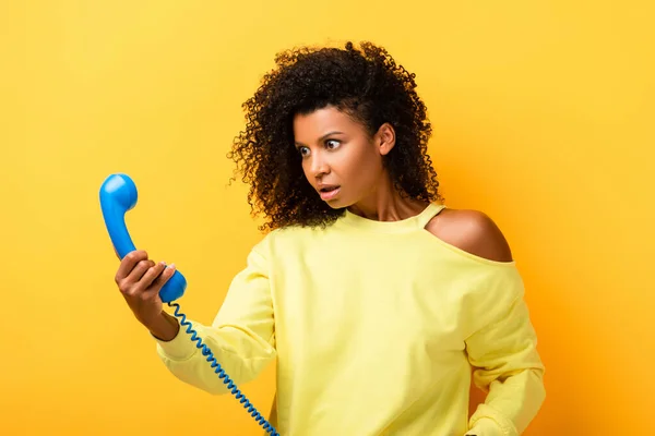 Femme afro-américaine choquée regardant le téléphone vintage sur jaune — Photo de stock