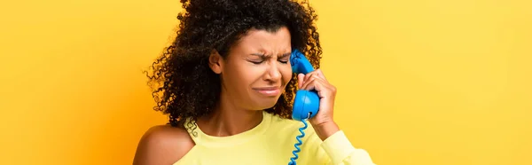 Femme afro-américaine bouleversée parlant sur téléphone vintage sur jaune, bannière — Photo de stock