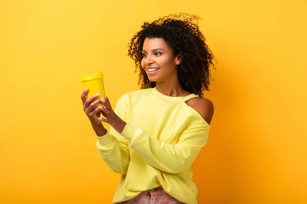 Alegre afroamericana mujer celebración reutilizable eco taza en amarillo - foto de stock