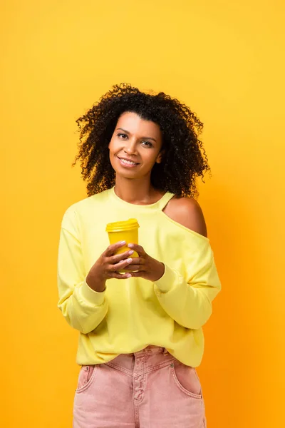 Glücklich afrikanisch-amerikanische Frau hält Mehrwegbecher auf gelb — Stockfoto