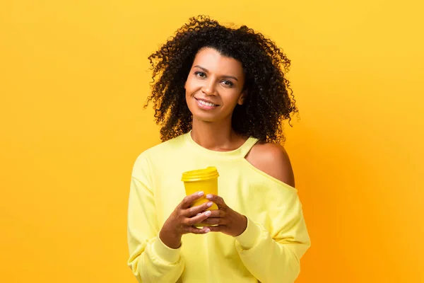 Souriant afro-américaine tenant tasse réutilisable sur jaune — Photo de stock