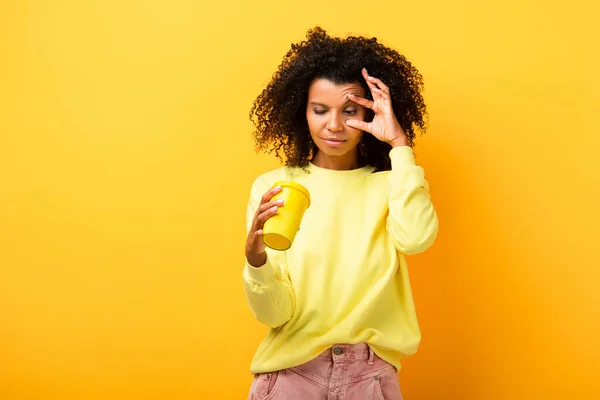 African american woman holding and looking at reusable cup on yellow — Stock Photo