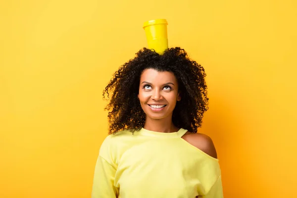 Happy african american woman with reusable cup on head on yellow — Stock Photo