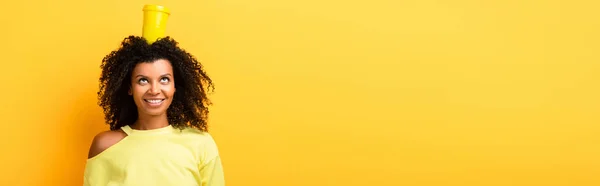 Happy african american woman with reusable cup on head on yellow, banner — Stock Photo