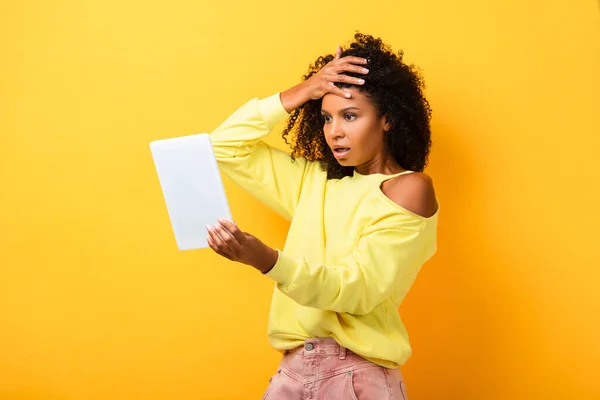 Shocked african american woman looking at digital tablet on yellow — Stock Photo