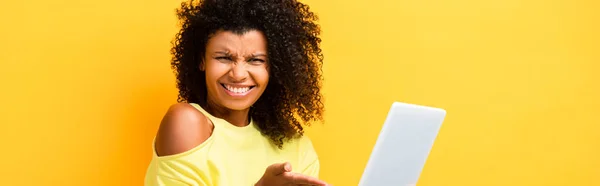 Skeptische afrikanisch-amerikanische Frau zeigt mit der Hand auf digitales Tablet auf gelb, Banner — Stockfoto