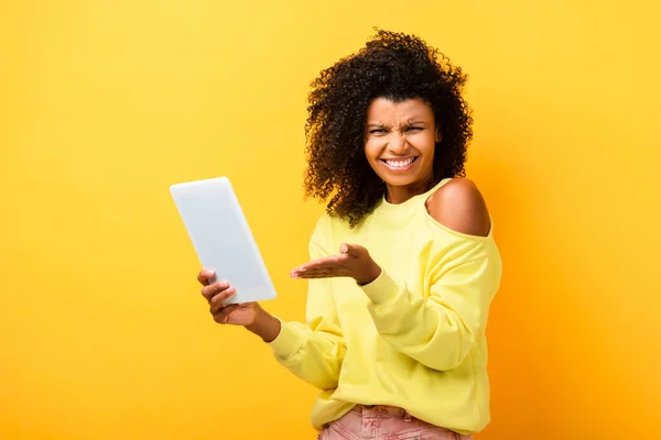 Mulher afro-americana cético apontando com a mão para tablet digital em amarelo — Fotografia de Stock