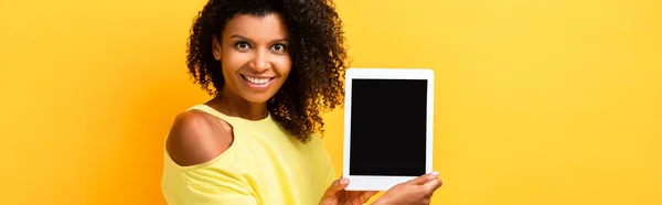 Happy african american woman holding digital tablet with blank screen on yellow, banner — Stock Photo