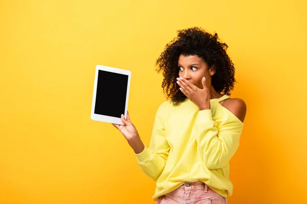 Chocado Africano americano mulher olhando para tablet digital com tela em branco no amarelo — Fotografia de Stock