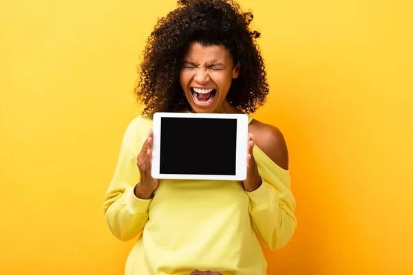 Mulher africana americana segurando tablet digital com tela em branco e gritando em amarelo — Fotografia de Stock