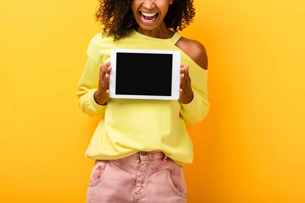 Vista recortada de mujer afroamericana sosteniendo tableta digital con pantalla en blanco en amarillo - foto de stock