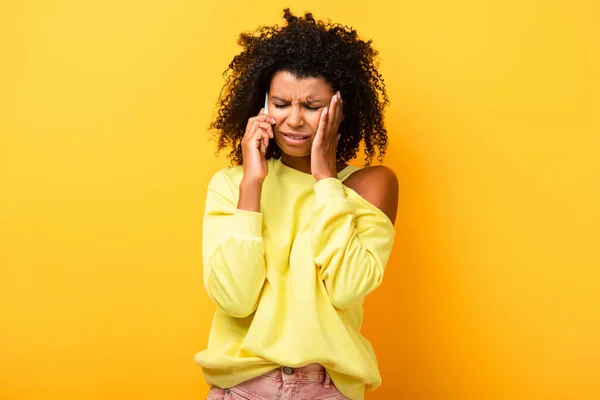 Mujer afroamericana triste hablando en teléfono inteligente en amarillo - foto de stock