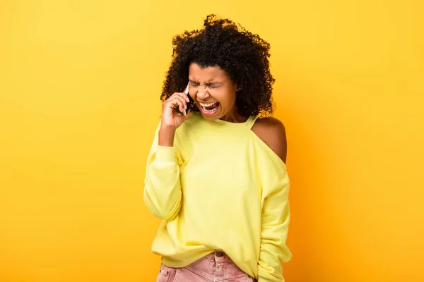 Angry african american woman holding smartphone and screaming on yellow — Stock Photo