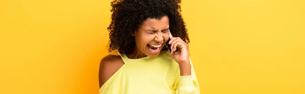 Femme afro-américaine en colère tenant smartphone et criant sur jaune, bannière — Photo de stock