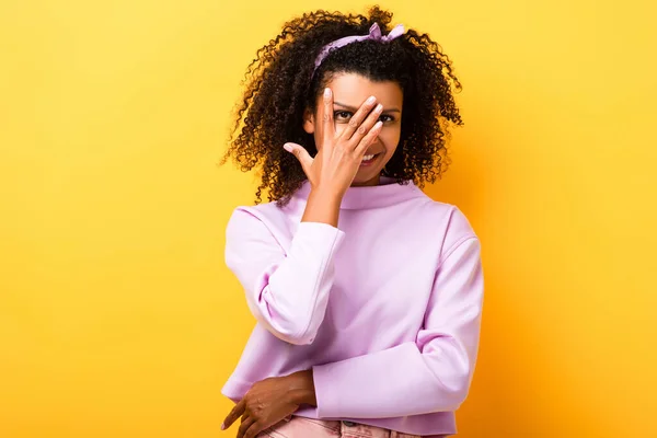 Happy african american woman covering face with hand on yellow — Stock Photo